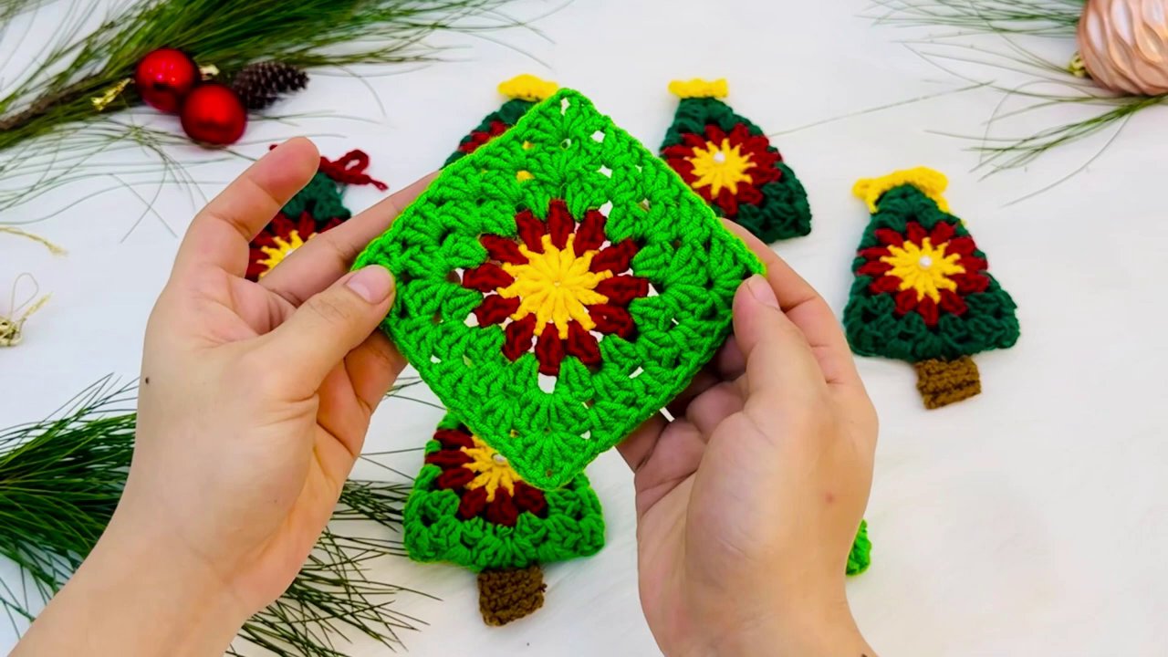 Craft a Festive Granny Square Christmas Tree: A Step-by-Step Crochet Tutorial 2 A close-up of fair-skinned hands holding a red yarn and a yellow crochet hook against a plain white background, with the text "ROUND 2 GRANNY SQUARE" visible.