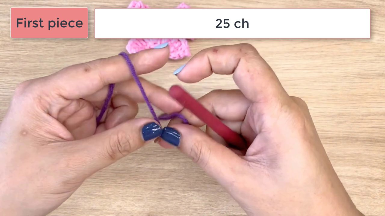 Master the Art of Crochet: A Step-by-Step Guide to Crafting a Beautiful Bow 2 A pair of hands with blue-painted fingernails holds a red crochet hook and purple yarn, ready to begin on a light wooden surface.