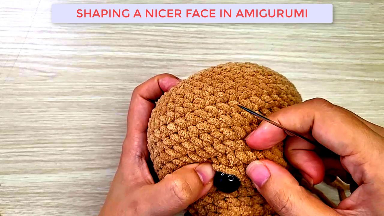 Mastering Amigurumi: A Step-by-Step Guide to Shaping and Embroidering a Dog's Face 3 The head is turned to show the back, where a yarn tail is being secured and woven in neatly.