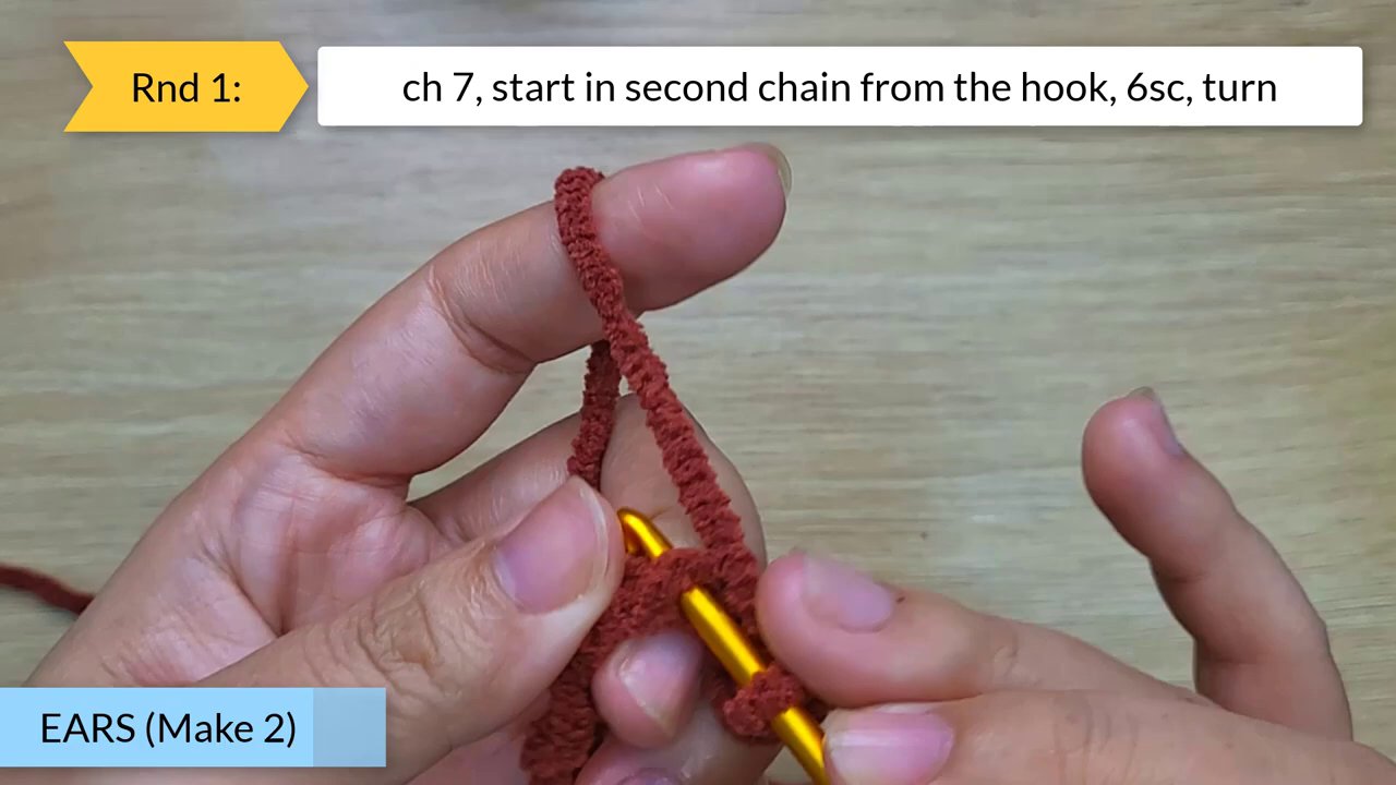 Craft Your Own Adorable Crochet Dog Bun: A Beginner's Step-by-Step Guide 5 A hand holds the white crochet piece with attached red ears, using a black tool to secure a safety eye in place.