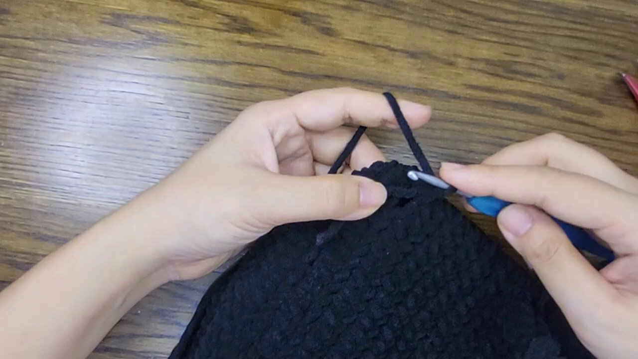 Crafting Comfort: A Step-by-Step Guide to Crocheting Your Own Bicycle Seat Post Cover 5 The hands continue working, with several completed rows of the black tube now visible.