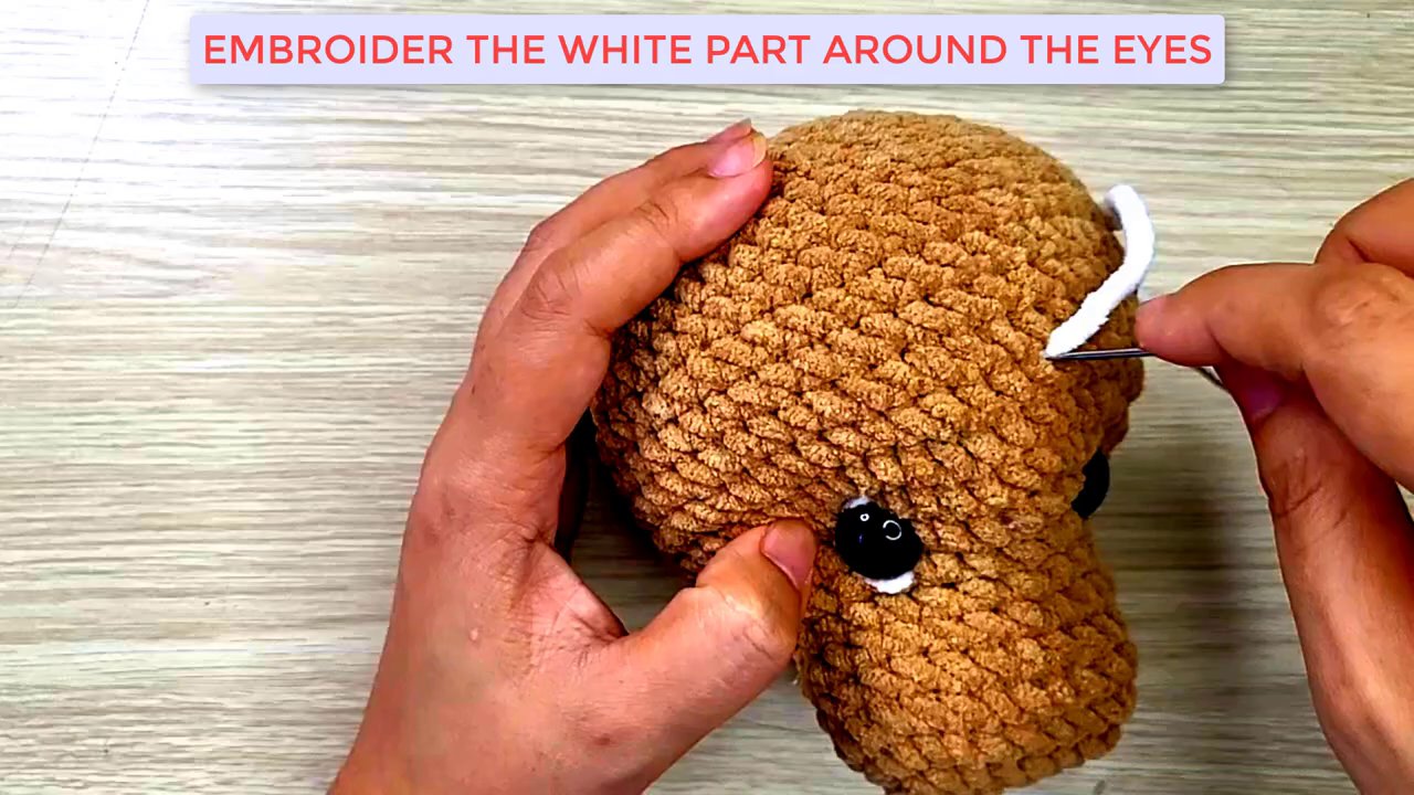 Mastering Amigurumi: A Step-by-Step Guide to Shaping and Embroidering a Dog's Face 7 The white embroidery is partially complete, showing a crescent shape taking form beneath the black eye.