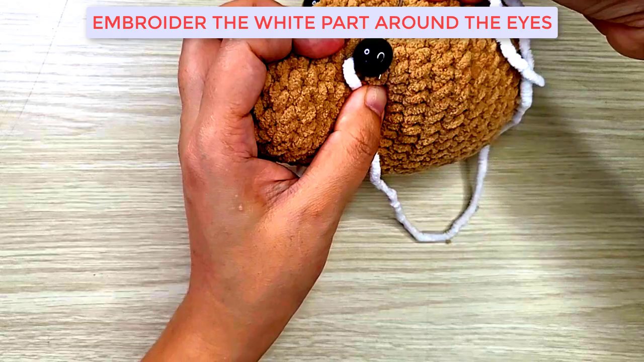 Mastering Amigurumi: A Step-by-Step Guide to Shaping and Embroidering a Dog's Face 9 The completed dog head rests on the wooden surface, showcasing a friendly, fully shaped and embroidered face ready for the next part of the tutorial.