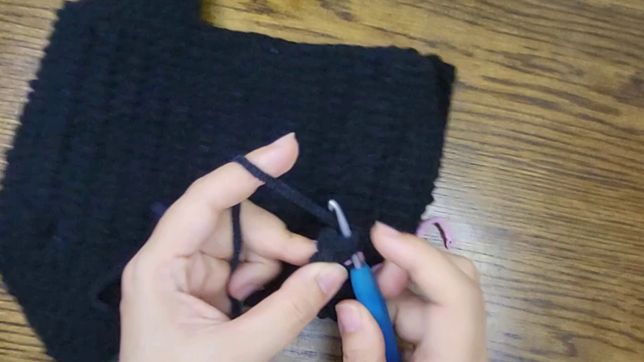 Crafting Comfort: A Step-by-Step Guide to Crocheting Your Own Bicycle Seat Post Cover 9 The final frame shows the hands pausing mid-stitch, with the elongated black cover resting on the wooden surface, a testament to the completed work.